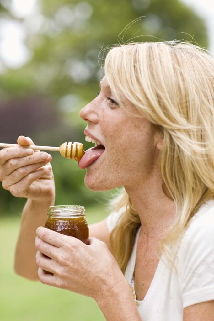 woman enjoying licking honey off a honey spoon